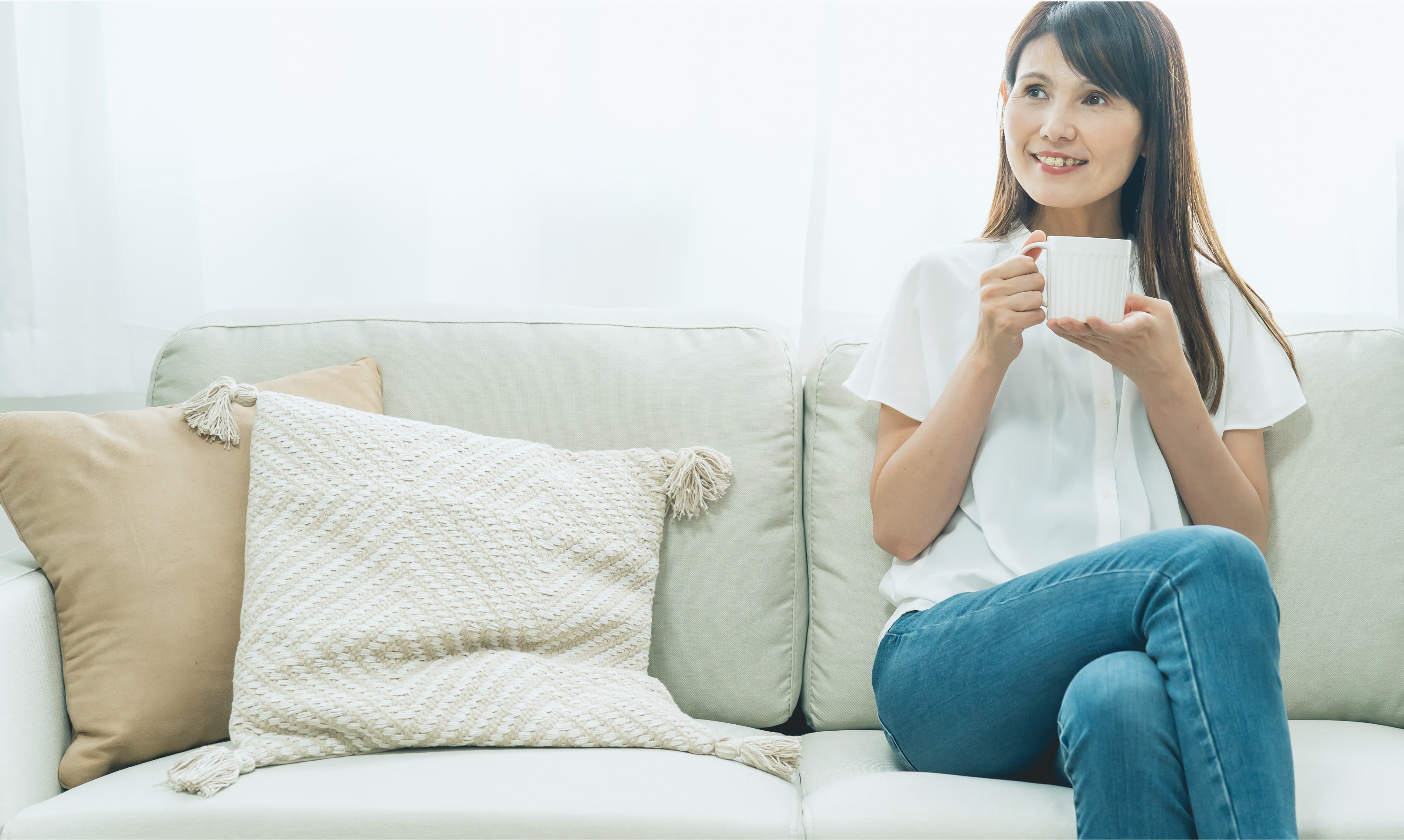 ソファでくつろぎながらカップを持つ女性
